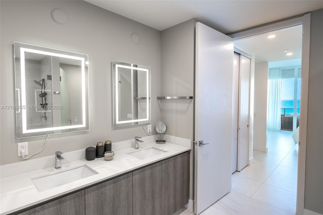 Bathroom featuring a double vanity with integrated rectangular sinks, white stone-finish countertop, dual backlit mirrors, and gray wood-finish cabinetry