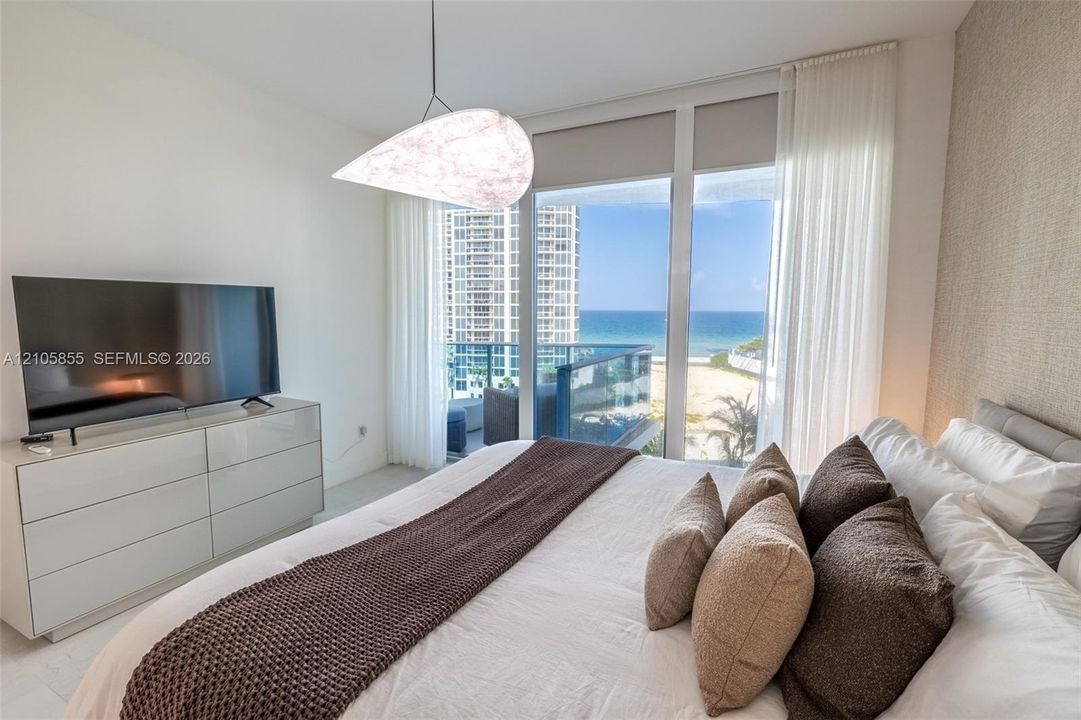 Floor-to-ceiling windows, sculptural pendant light, textured accent wall, and balcony featuring ocean and beach scenery
