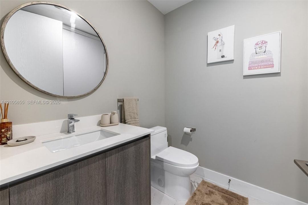 Floating vanity featuring a wood-finish cabinet and solid-surface countertop, integrated rectangular sink, chrome-finish faucet, and oval wall-mounted mirror