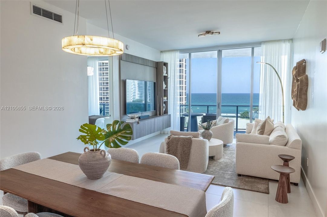 Open-concept living space featuring floor-to-ceiling windows, built-in media cabinetry, a modern circular chandelier, and direct balcony access with ocean horizon backdrop