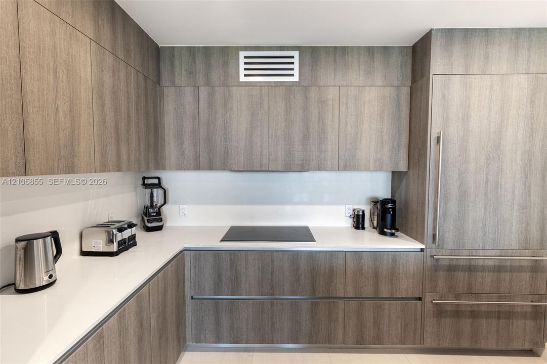 Contemporary kitchen featuring flat-panel wood-finish cabinetry, white solid-surface countertops, a seamless back-painted glass backsplash, a built-in induction cooktop, and a panel-ready refrigerator