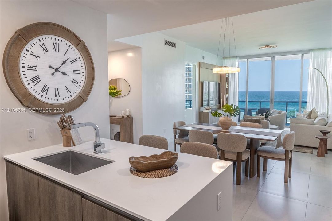 Kitchen island featuring a white countertop, under-mount sink, and modern faucet, complemented by wood-finish cabinetry and large-format tile flooring, complete with floor-to-ceiling glass sliding doors