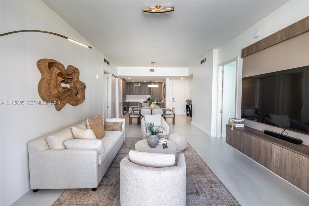 Open-concept living space featuring a custom wall-mounted wood-finish media console, recessed lighting, and tile flooring throughout