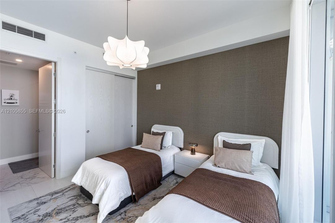 Textured accent wall, sliding door closet with neutral finish, sculptural pendant lighting, and stone-finish tile flooring