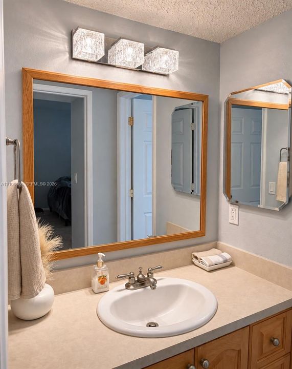 Bathroom vanity featuring a solid-surface countertop, an integrated drop-in sink, wood-finish cabinetry, a framed vanity mirror, and three-light geometric wall-mounted fixture