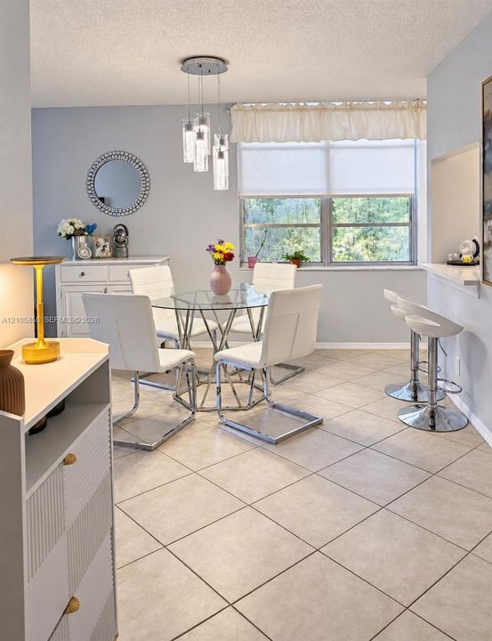 Dining area featuring large-format ceramic tile flooring, a multi-pendant glass light fixture, and a built-in kitchen pass-through counter