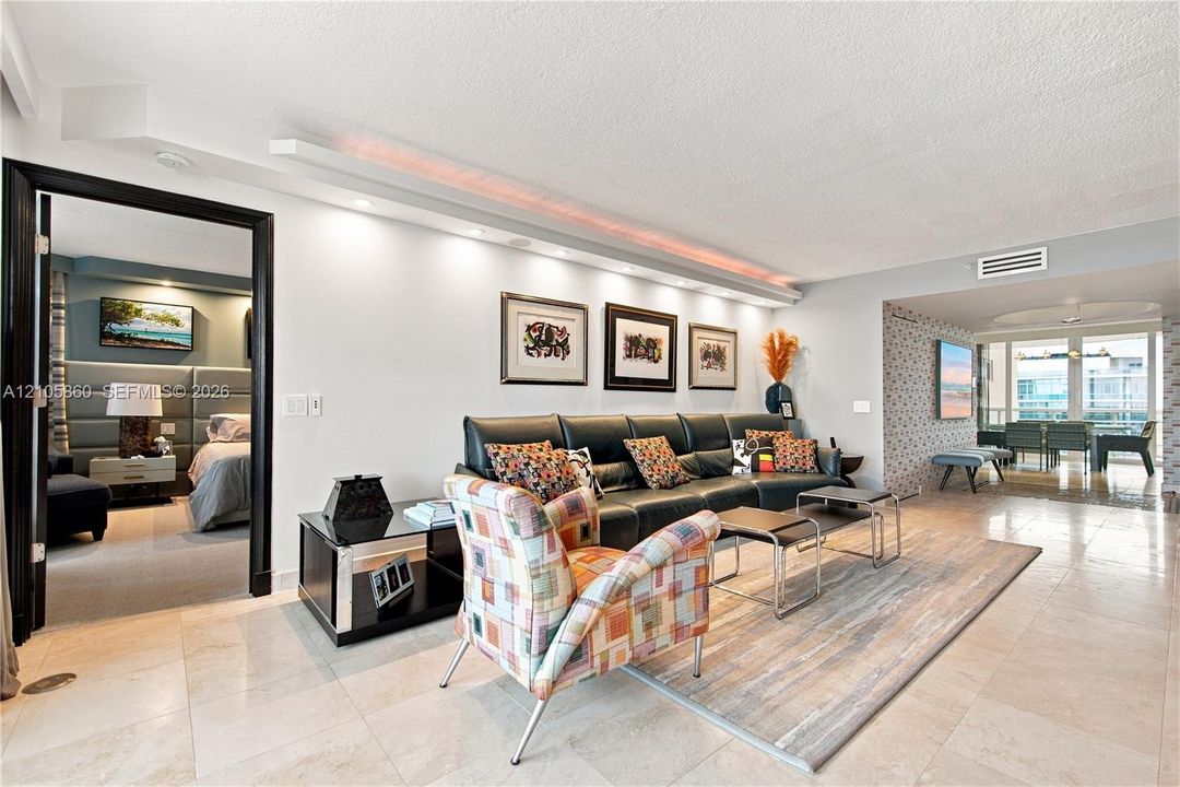 Open-concept living area featuring stone tile flooring, built-in cove lighting, and a distinct entryway with high-contrast black trim