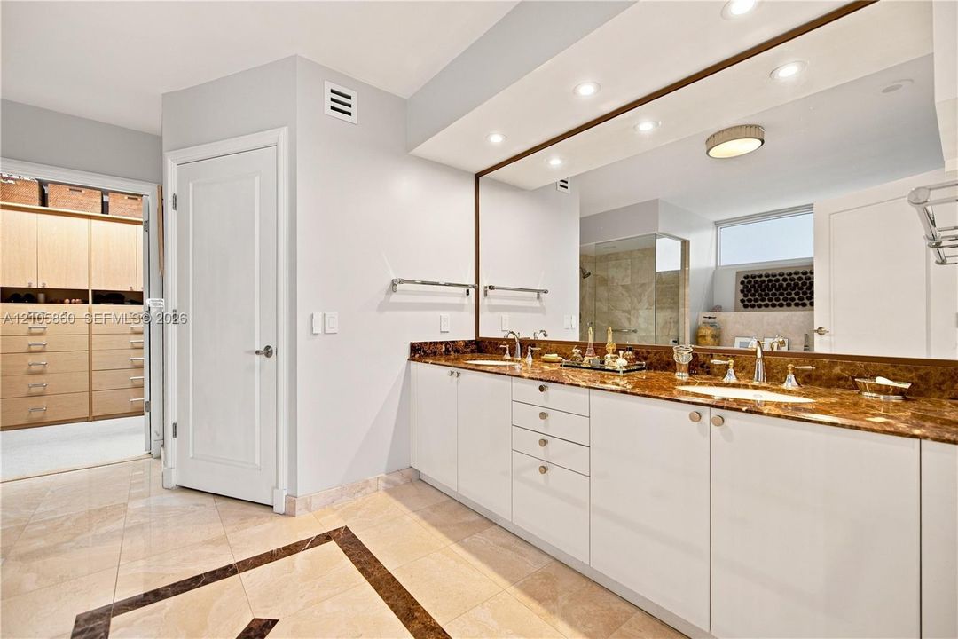 Dual-sink vanity with stone countertop, polished metal fixtures, recessed ceiling lighting, full-width vanity mirror, and built-in closet cabinetry