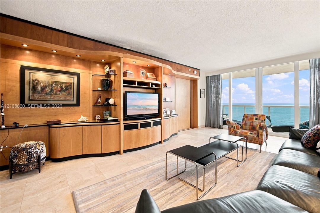 Built-in floor-to-ceiling wood cabinetry with integrated lighting, tile flooring, and floor-to-ceiling windows featuring ocean scenery