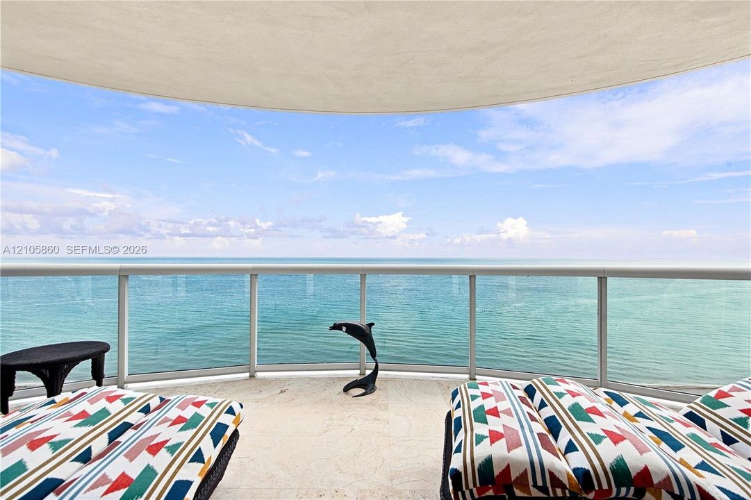 Curved private balcony featuring stone flooring and a glass panel railing overlooking the ocean