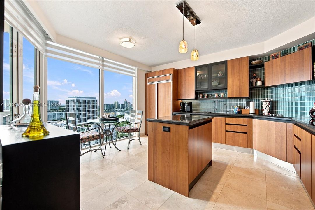 Kitchen featuring wood-veneer cabinetry, stone countertops, a central island, tile flooring, and floor-to-ceiling windows