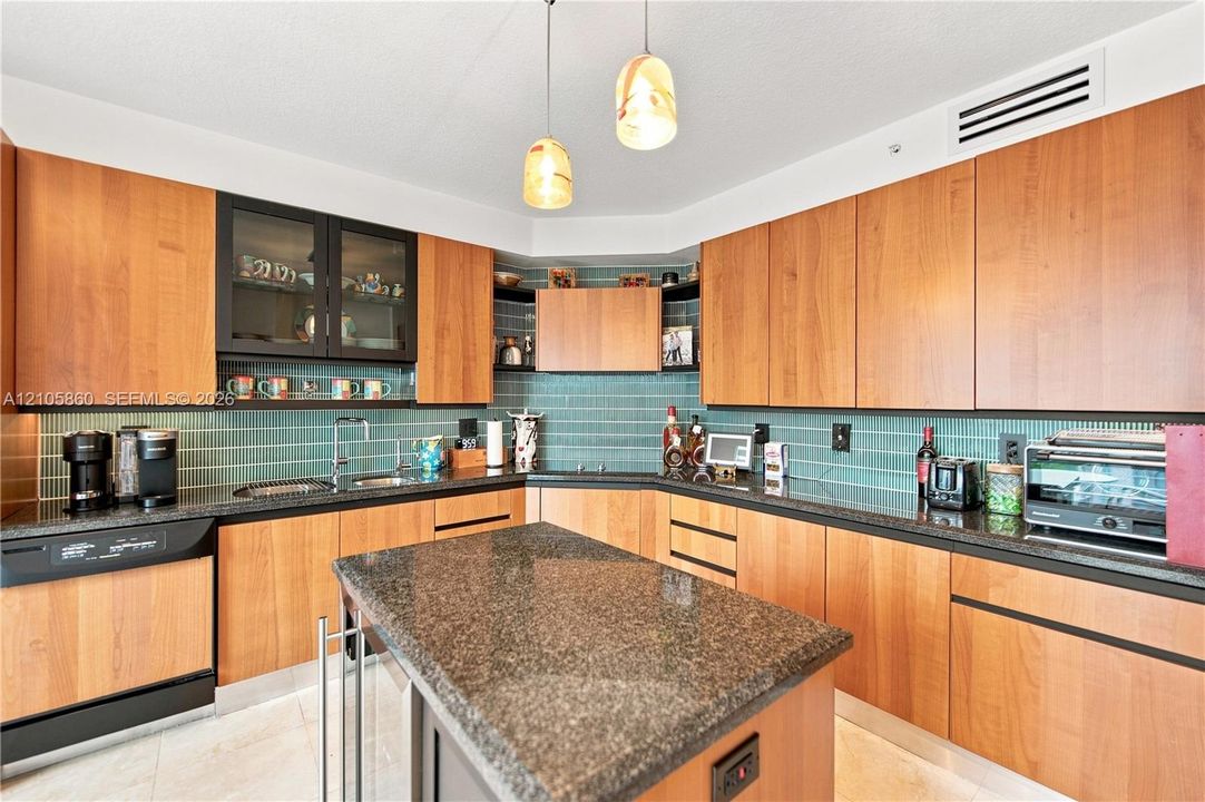 Kitchen featuring custom wood cabinetry, dark stone countertops, a central island, blue subway tile backsplash, and dual pendant lighting