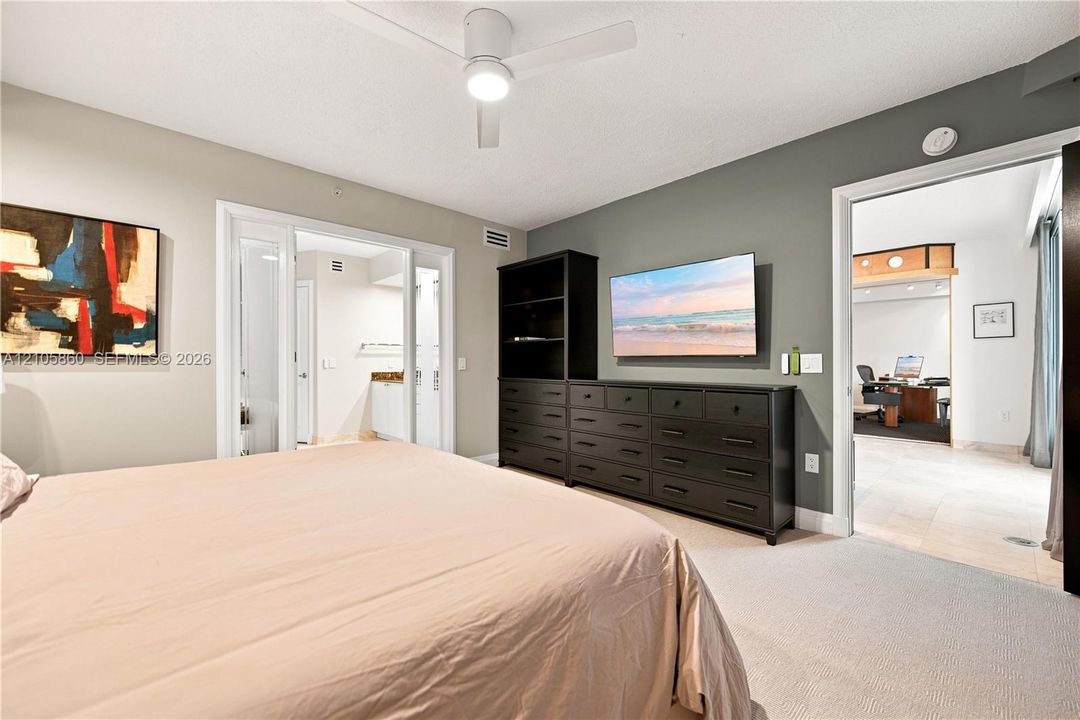 Neutral-toned room featuring a white ceiling fan with integrated lighting, wall-to-wall carpeting, and a dark-finished built-in cabinetry unit