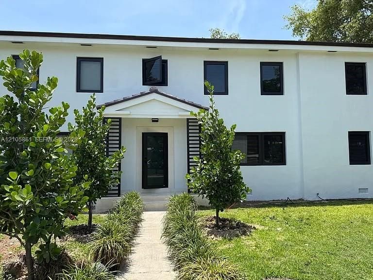 Two-story exterior featuring a white smooth-finish facade, dark-framed casement windows, a gabled front entryway, and metal slat architectural detailing