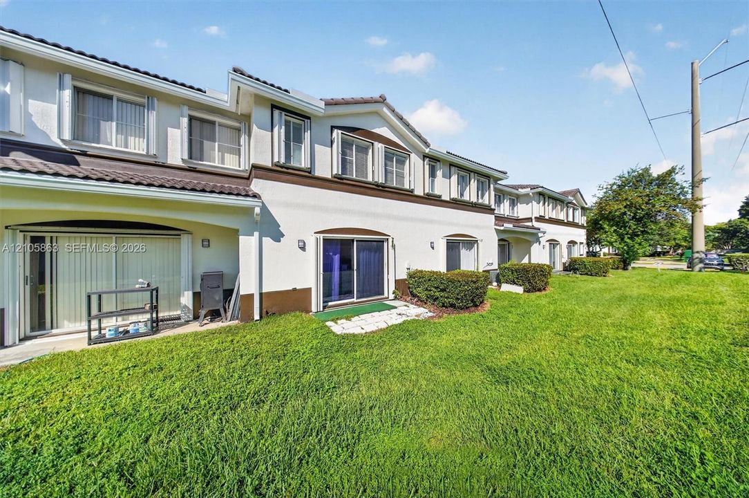 Multi-unit exterior featuring a stucco facade, dark-toned roof shingles, sliding glass doors, and established landscaping