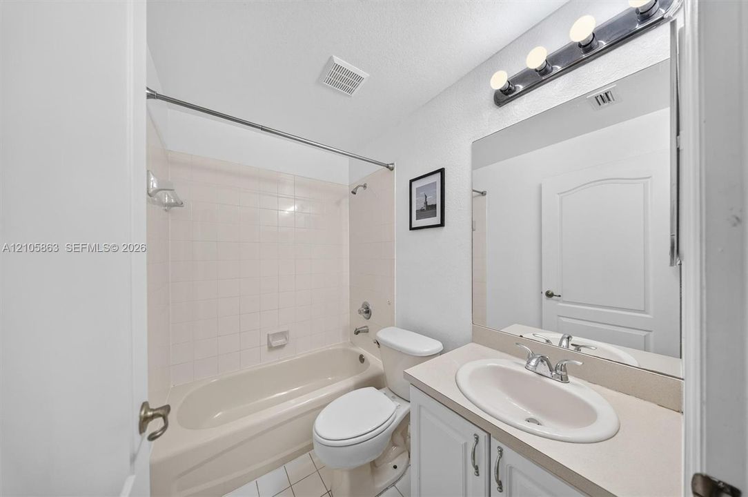 Full bathroom featuring a white vanity with a neutral solid-surface countertop, integrated oval sink, chrome dual-handle faucet, and an oversized wall mirror with a multi-bulb light fixture