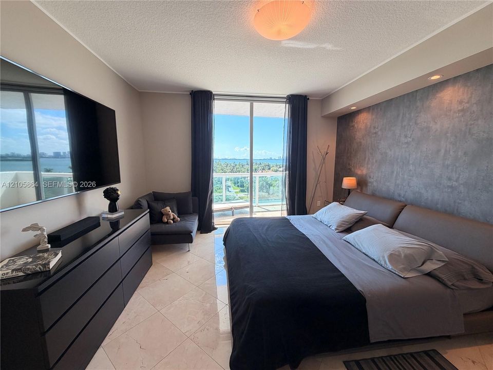 Floor-to-ceiling sliding glass doors opening to a balcony, large-format tile flooring, textured accent wall, and recessed ceiling lighting