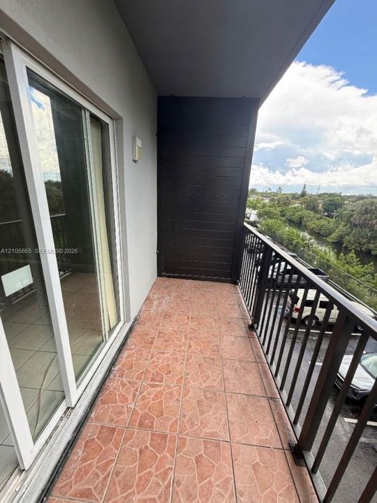 Covered balcony featuring multi-tonal stone-tile flooring, dark horizontal wood-plank accent siding, and black metal railings