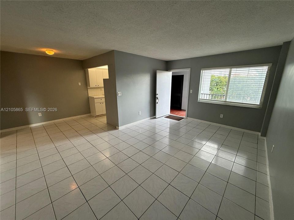 Neutral-toned interior featuring large-format white tile flooring, white cabinetry with recessed-panel doors, and a window with horizontal blinds