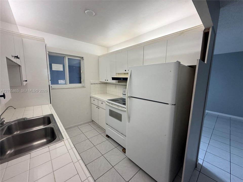 Kitchen featuring white cabinetry, ceramic tile countertops, double-basin stainless steel sink, tile flooring, and white appliance suite