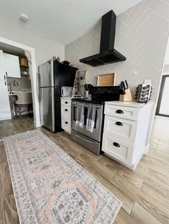 Main House Kitchen featuring white shaker-style cabinetry with matte black hardware, herringbone-patterned wall tile, stainless steel appliances, and wood-finish flooring