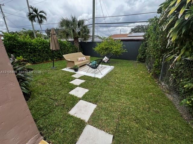 Private backyard featuring a manicured lawn, concrete paver pathway, elevated concrete patio, mature palms, and opaque perimeter fencing