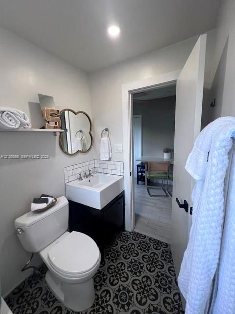 Bathroom featuring patterned floor tile, square vessel sink with wall-mounted faucet, subway tile backsplash, and wall-mounted storage shelving