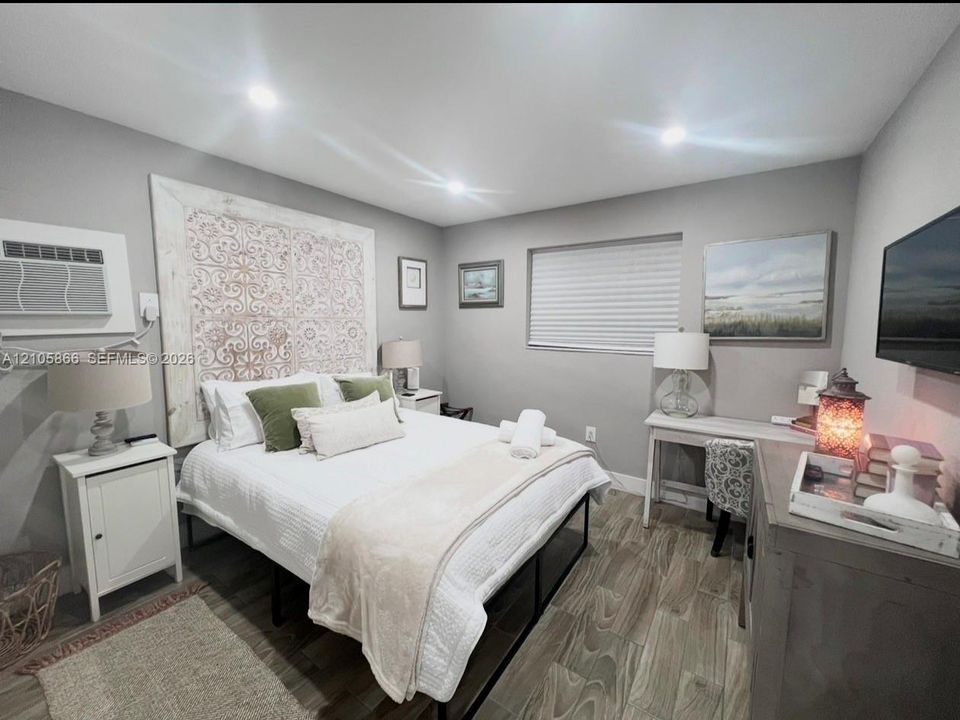 Main house bedroom 1 Neutral-toned walls, wood-finish flooring, recessed lighting, and a decorative wall-mounted accent panel