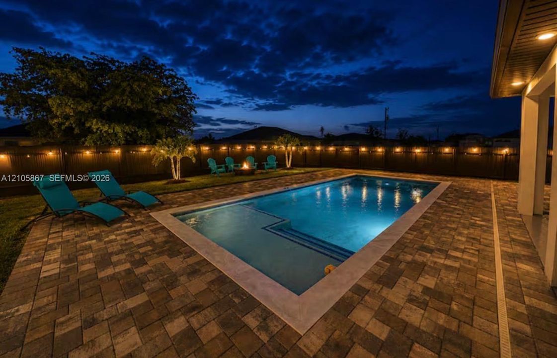 Backyard featuring a concrete-paved patio, rectangular in-ground pool with integrated entry steps, manicured lawn, and perimeter privacy fencing