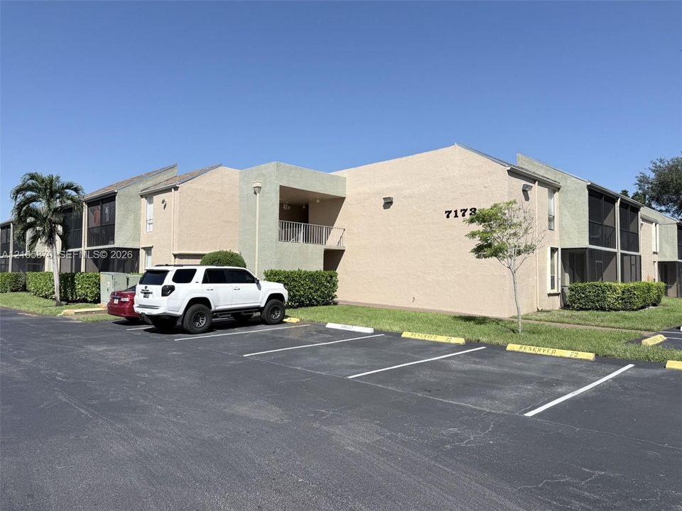 Multi-level exterior featuring a stucco facade, covered balconies, screened enclosures, and asphalt parking area