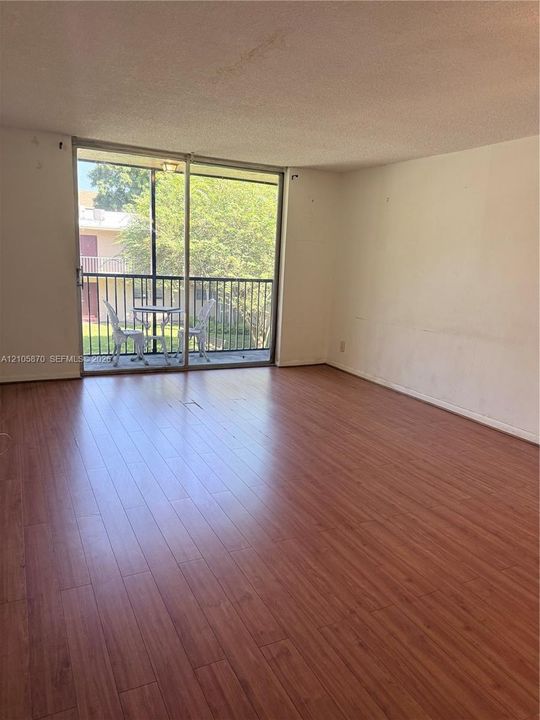 Living space featuring wood-finish flooring and a large sliding glass door opening to a screened balcony with metal railings