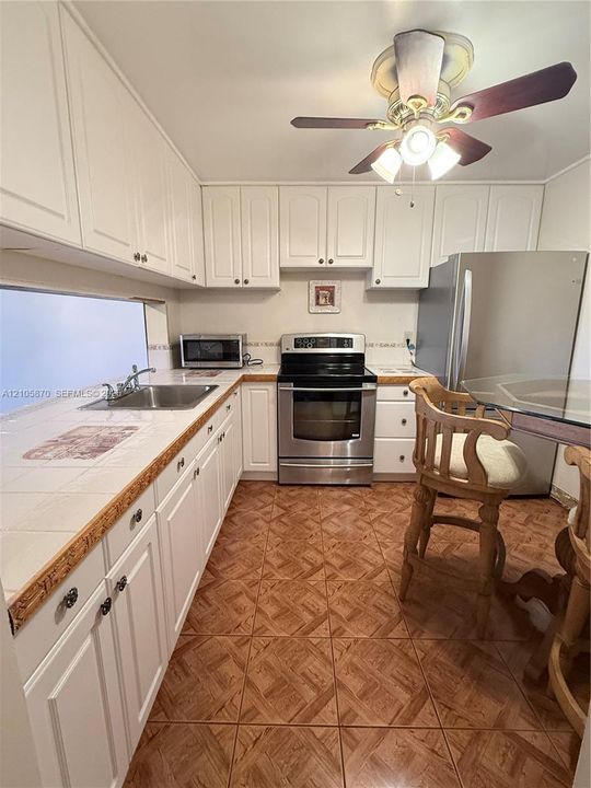 Kitchen featuring white cabinetry, tile countertops, stainless steel appliances, a stainless steel sink with a dual-handle faucet, and tile flooring