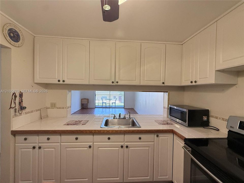 Kitchen featuring white raised-panel cabinetry, tiled countertops, stainless steel dual-basin sink, and built-in microwave