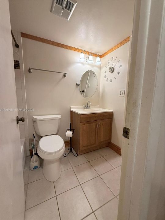 Bathroom featuring ceramic tile flooring, a wood-finish vanity with a surface-mounted sink, a three-light fixture, and an oval wall-mounted mirror