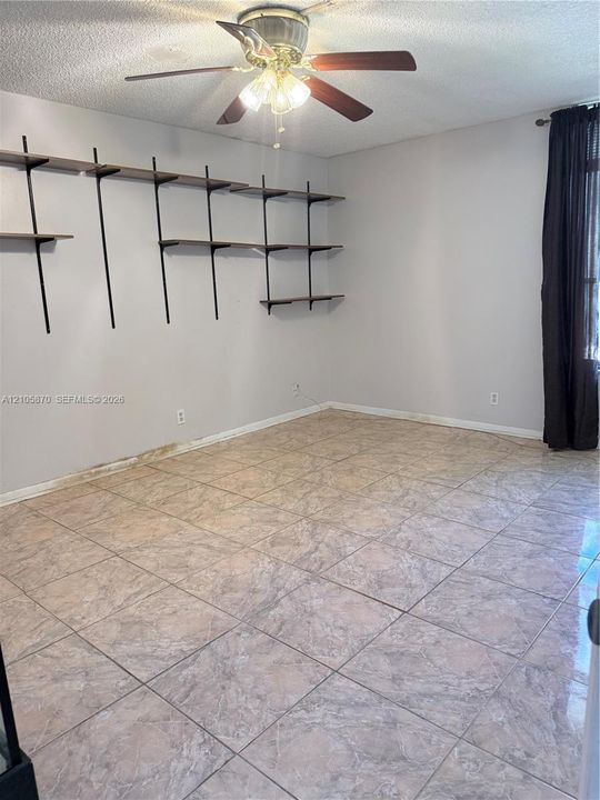 Room featuring large-format ceramic tile flooring, wall-mounted tiered shelving, and a ceiling fan with integrated lighting