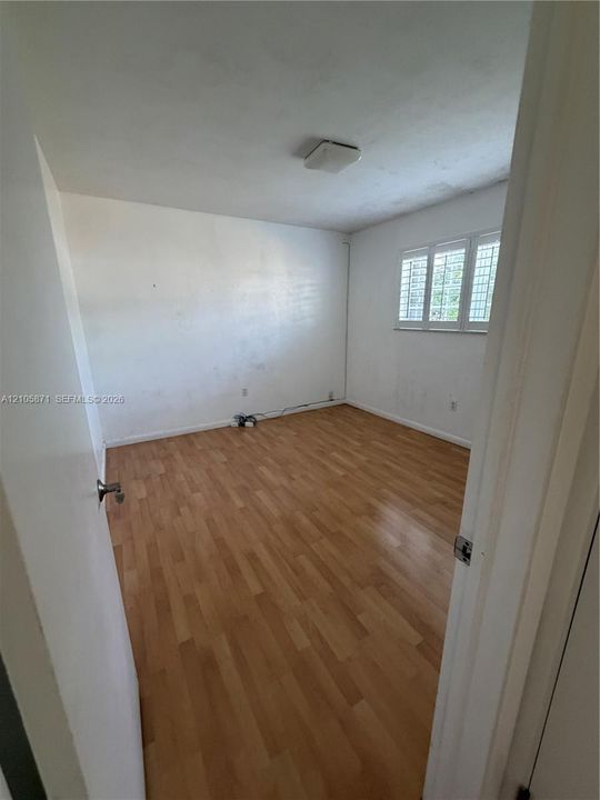 Room featuring wood-finish flooring, white walls, and a multi-pane window with adjustable shutters