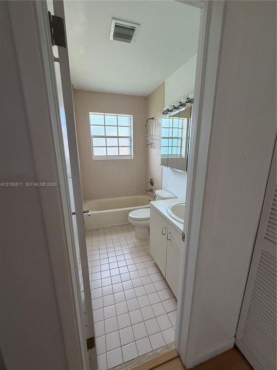 Bathroom featuring ceramic tile flooring, a built-in vanity with a stone countertop and integrated sink, a tiled tub surround, and a multi-light fixture