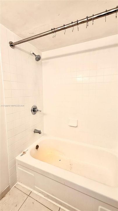Bathtub and shower combination featuring white tiled surround, chrome plumbing fixtures, and integrated soap dish