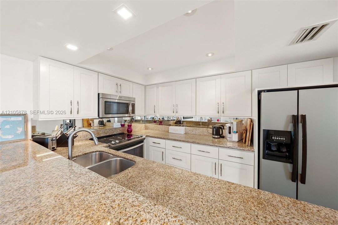 Kitchen featuring white shaker-style cabinetry, expansive stone countertops, stainless steel appliances, a double-basin undermount sink, and mirrored backsplash