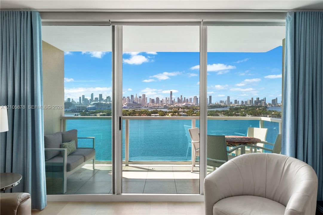 Floor-to-ceiling sliding glass doors, private balcony, tile balcony flooring, and glass railing, featuring a coastal and urban skyline backdrop