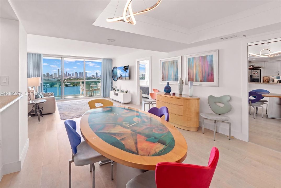 Open-concept interior featuring light wood-finish flooring, floor-to-ceiling glass sliding doors, recessed tray ceiling lighting, and a modern sculptural chandelier
