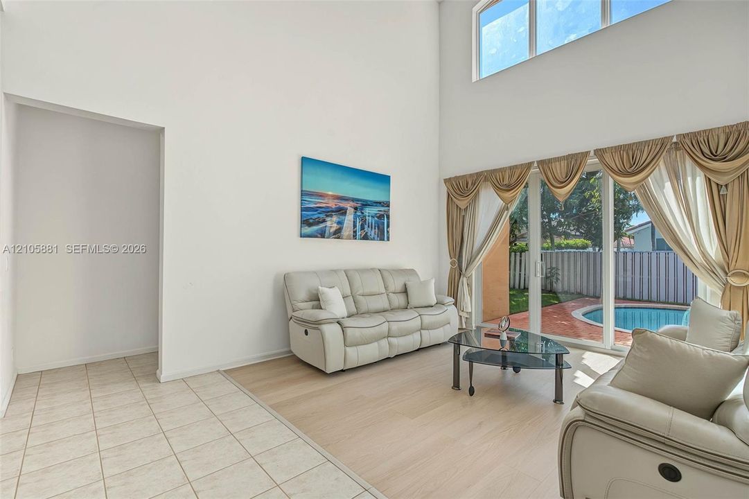 High ceilings with transom windows, neutral tile and wood-finish flooring, and glass sliding doors providing exterior exposure to a swimming pool