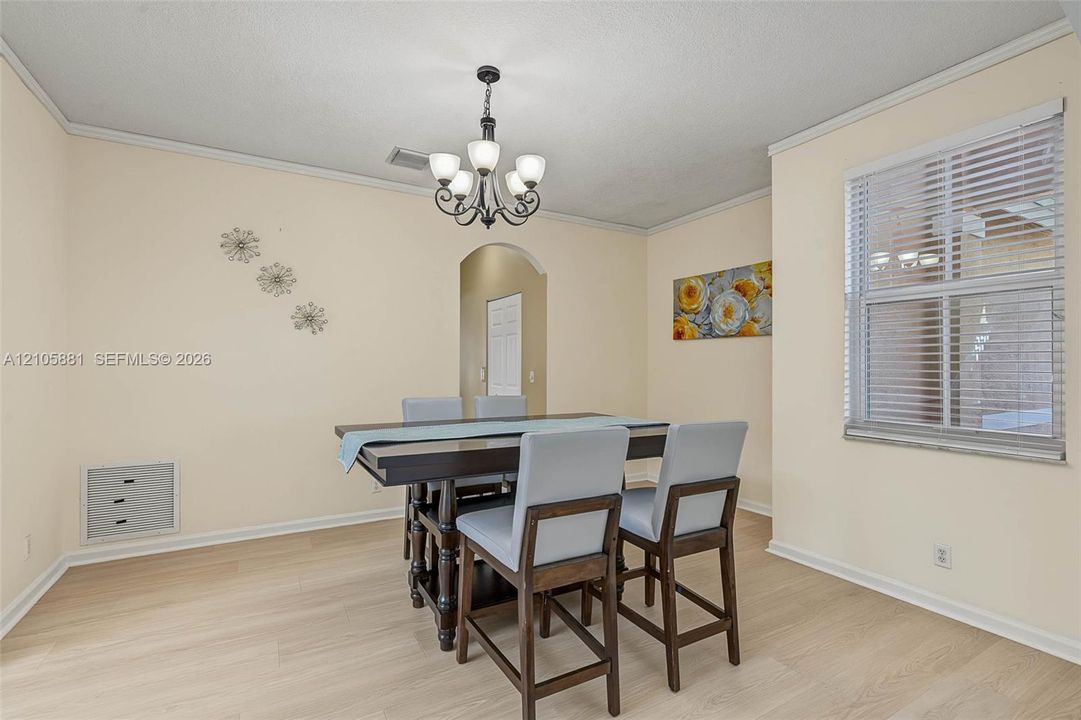 Dining area featuring light-toned wood-finish flooring, a wrought iron chandelier with frosted glass shades, crown molding, and an arched entryway