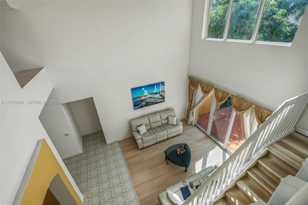 High-ceilinged living area featuring wood-finish flooring, floor-to-ceiling windows, and staircase with a white wood balustrade