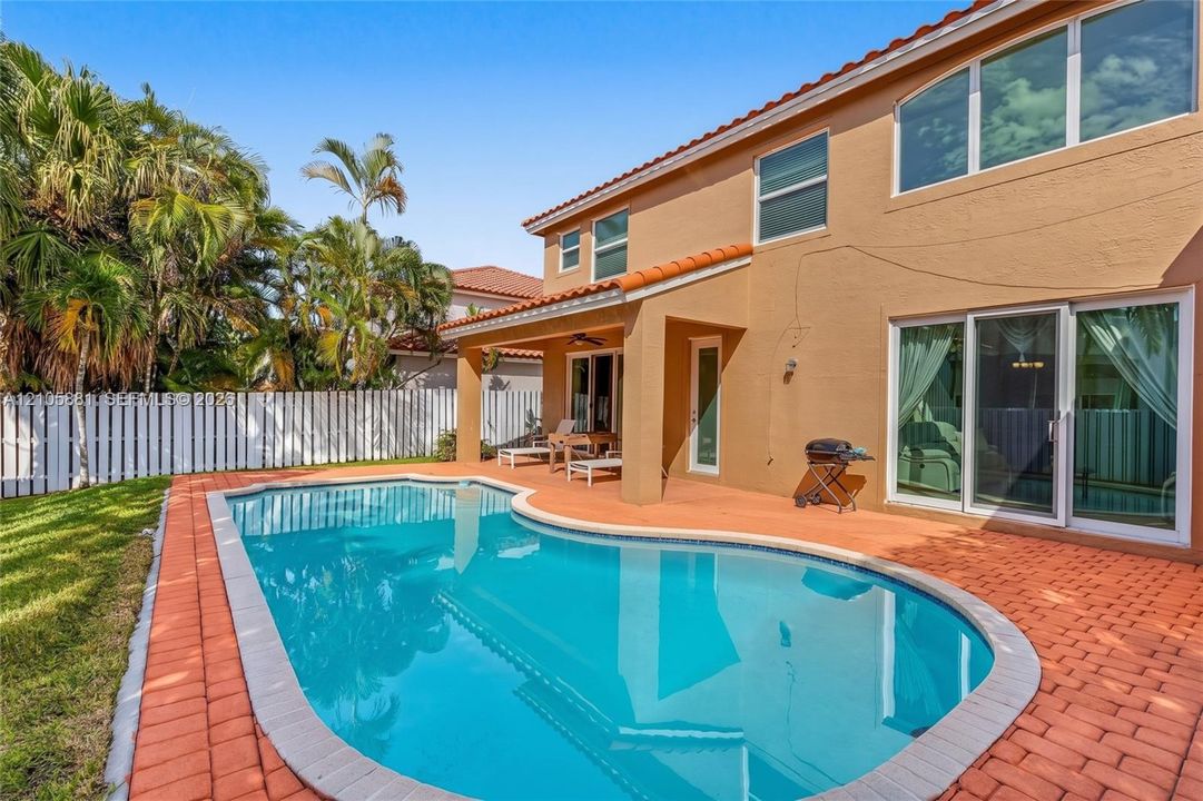 Stucco exterior featuring a tiled roof, covered patio, paver hardscaping, and an in-ground pool enclosed by a privacy fence
