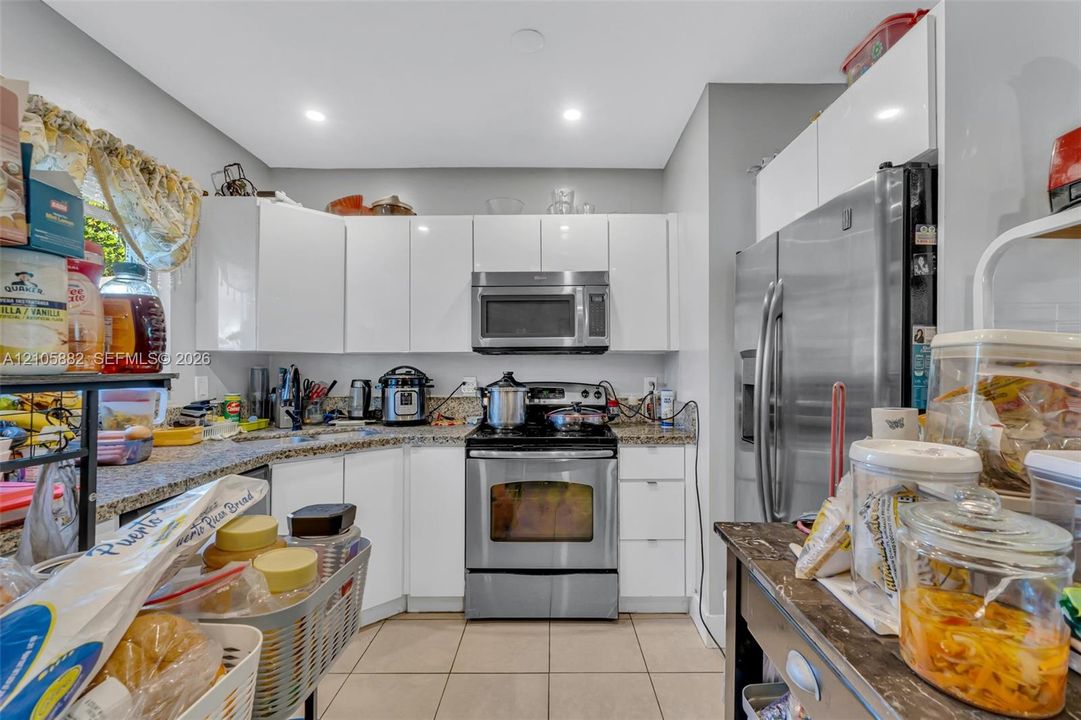Kitchen featuring high-gloss white cabinetry, speckled stone countertops, stainless steel appliances, and tile flooring