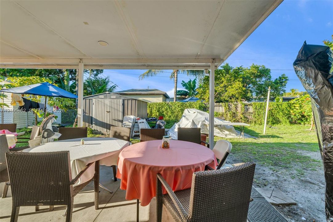 Covered concrete patio featuring structural support posts, metal overhead roofing, and a fenced backyard area with an exterior storage structure