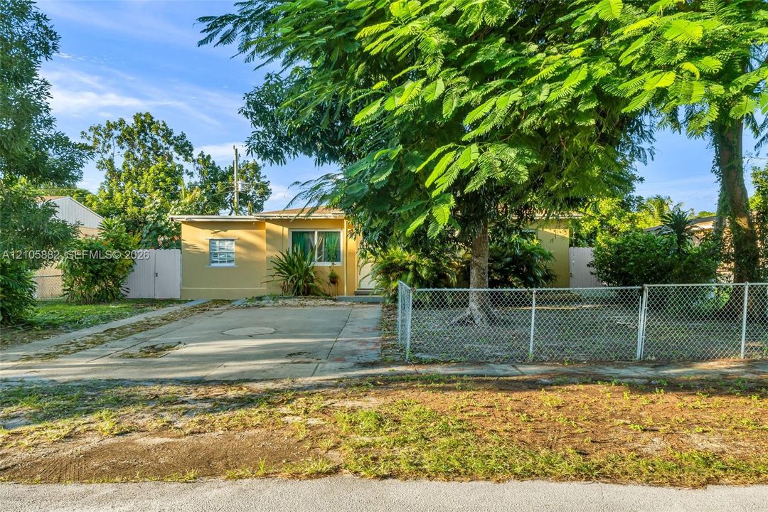 Single-story residence featuring a paved driveway, chain-link perimeter fencing, and mature landscaping