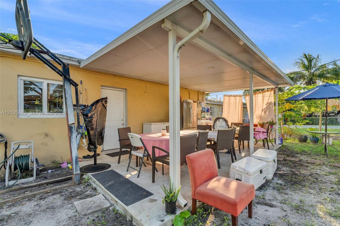Covered outdoor patio featuring a concrete slab foundation, white structural support pillars, and exterior-grade lighting