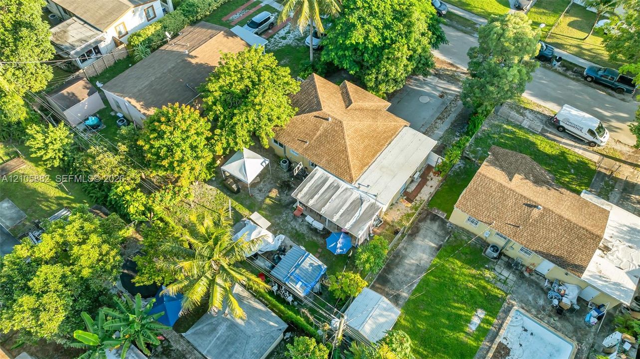 Aerial perspective featuring a residential property with a shingled hip roof, paved driveway, mature trees, and landscaping